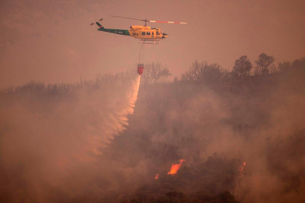 A helicopter is pictured from Alhaurin de la Torre as it drops water over a wildfire in Sierra de Mijas mountain range in Malaga province on July 15, 2022. AFPPIX