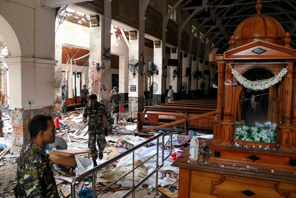 Sri Lankan security personnel walk past dead bodies covered with blankets amid blast debris at St. Anthony's Shrine following an explosion in the church in Kochchikade in Colombo on April 21, 2019. — AFP