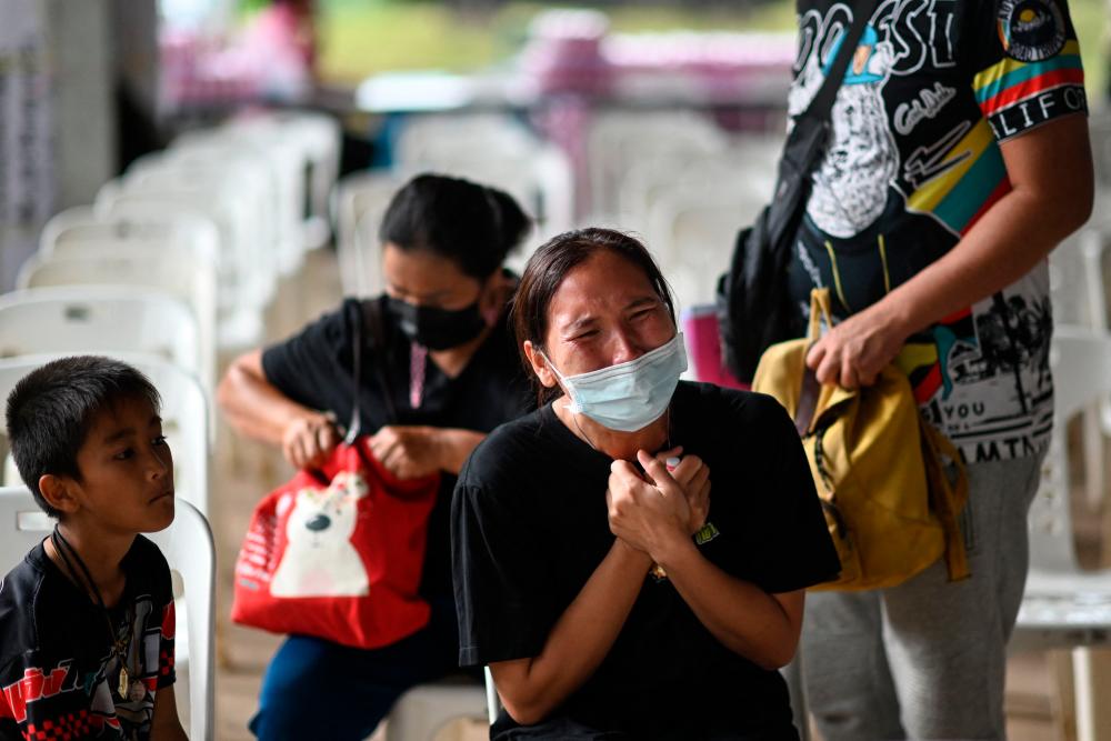 A child sits next to the mother of a victim as she cries outside the nursery, where a former police officer killed at least 37 people in a mass shooting, in Thailand’s northeastern Nong Bua Lam Phu province on October 7, 2022. AFPPIX