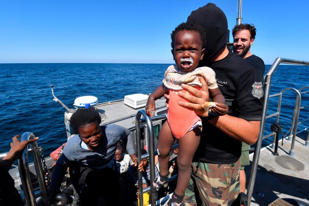 Migrants of African origin trying to flee to Europe are transferred from a small boat belonging to the Tunisian coast guard onto a larger vessel, at sea between Tunisia and Italy, on August 10, 2023. AFPPIX