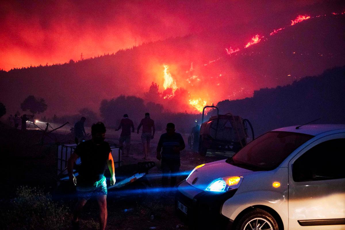 People and firefighters attempt to extinguish the flames as smoke and flares rise from a forested area following a wildfire in the Seferihisar district of Izmir, Turkey, on June 30, 2025 - AFPPIX