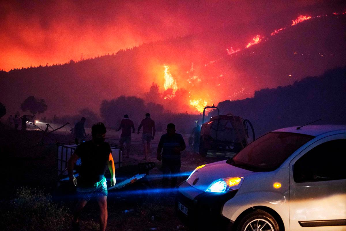 People and firefighters attempt to extinguish the flames as smoke and flares rise from a forested area following a wildfire in the Seferihisar district of Izmir, Turkey, on June 30, 2025. (Photo by Ahmet Ayberk Cimen / AFP)
