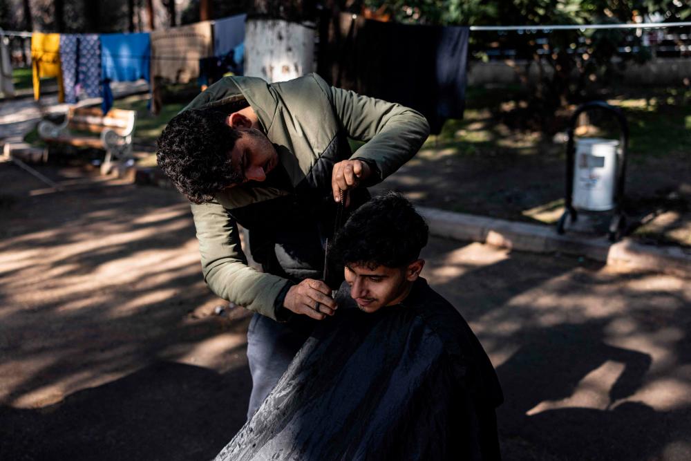 Eighteen-year-old Syrian Mohammed al-Hamo (L) cuts the hair of his 19-year-old brother Sobhi (R) in front of their tent at a makeshift camp in the city of Antakya on February 19, 2023. AFPPIX