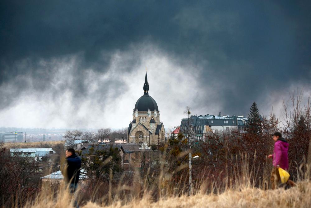 People walk in front of a church as smoke rises after an air strike in the western Ukrainian city of Lviv, on March 26, 2022. AFPPIX
