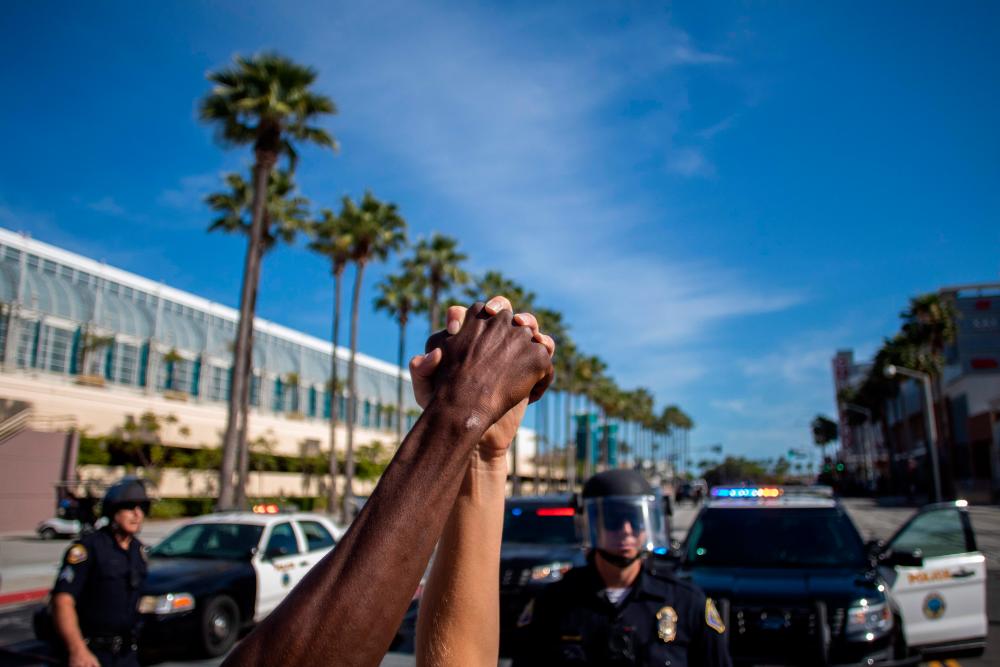 A black man and a white woman hold their hands up in a front of police officers in downtown Long Beach on May 31, 2020 during a protest against the death of George Floyd, an unarmed black man who died while being arrested and pinned to the ground by the knee of a Minneapolis police officer. — AFP