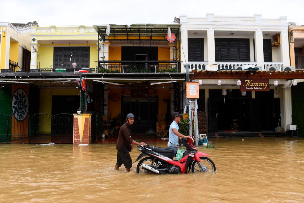 People push a motorbike in a flooded street following the passage of typhoon Noru in Hoi An city, Quang Nam province on September 28, 2022. AFPPIX