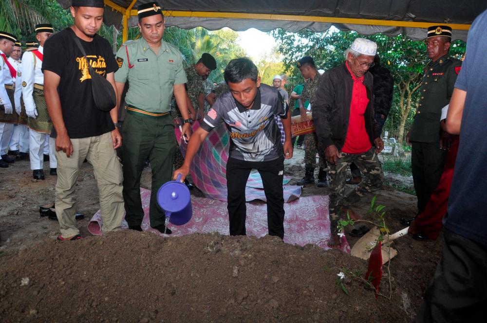 Muhammad Nabill Rozali, 14, anak tunggal Allahyarham Sarjan Rozali Abdul Rani, 39, menyiram air ke pusara bapanya sebaik selesai pengebumian anggota tentera terbabit di Tanah Perkuburan Islam Kampung Gong Bayor kira-kira 8 pagi tadi. - fotoBERNAMA