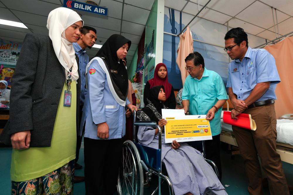 Cuepacs president Datuk Azih Muda presents a contribution for foot implant surgery to Nurul Nadirah Anuar, 14, a victim of an accident in Kampung Pakoh Jaya, Kuala Nerus on May 25. - Bernama