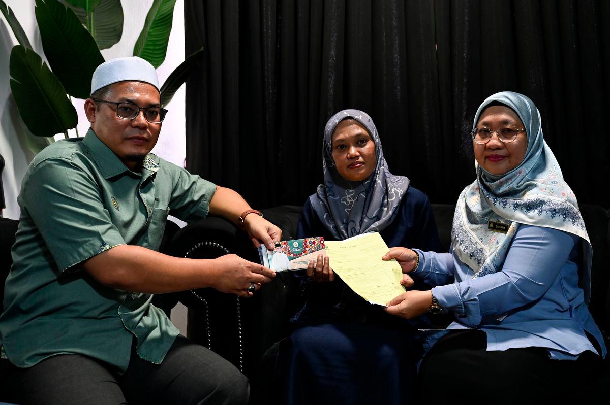Pengerusi Jawatankuasa Pembangunan Belia, Sukan dan Badan Bukan Kerajaan Negeri, Hishamuddin Abdul Karim (kiri), bersama Pengarah Pertubuhan Keselamatan Sosial (PERKESO) Terengganu, Suhara Mustaffa (kanan), menyampaikan faedah kepada Rusmailaili Samsuri, 43, (tengah), ibu kepada atlet angkat berat Sukan Malaysia (SUKMA) Terengganu, Allahyarham Siti Noralyaa Mat Marzuki, pada Majlis Penyampaian Faedah Pengurusan Mayat (FPM) di Taman Batin Perdana hari ini. - fotoBERNAMA