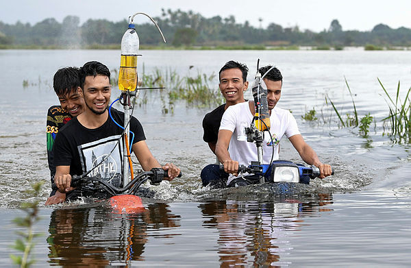 Ikram Shahidi Mat Kail, 24, (right) and his brother, Muhammad Zakaria, 22, (left) riding their modified bicycles through a flooded area in Kampung Banggol yesterday. — Bernama