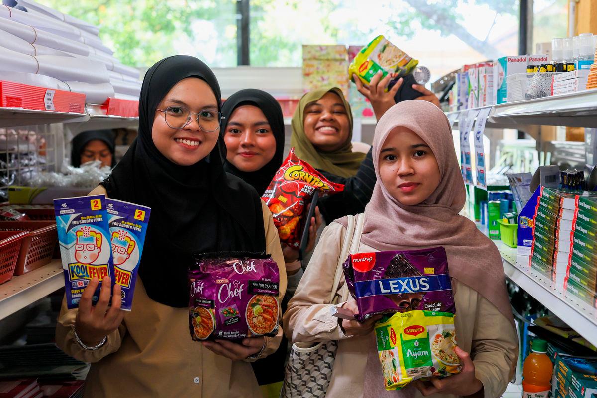 Penuntut Universiti Teknologi MARA (UiTM) Dungun Erina Natasha Mohd Saufi, 23, (kiri) bersama rakan menunjukkan bararangan keperluan harian yang dibeli menerusi Program Jualan Rahman MADANI (PJRM) @Kampus di UiTM Dungun, hari ini - BERNAMA