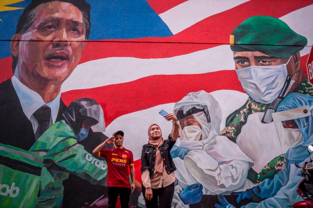 TRIBUTE TO HEROES... A couple takes a picture against the backdrop of a mural in Kuala Lumpur dedicated to the frontliners fighting the Covid-19 pandemic. ADIB RAWI YAHYA/THESUN