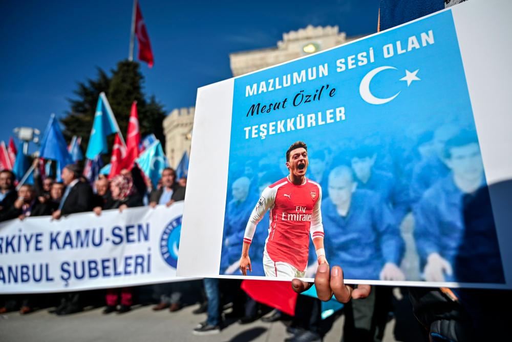 A supporter of China's Muslim Uighur minority holds a placard of Arsenal's Turkish origin German midfielder Mesut Ozil reading Thanks for being our voice past flags of East Turkestan during a demonstration at Beyazid square in Istanbul on Dec 14. — AFP