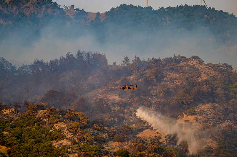 This photograph shows a helicopter dousing water to fight a forest fire in Turkey’s western province of Izmir on August 17, 2024. Firefighters are battling a strong forest fire in the Aegean resort city of Izmir for a third day, on August 17, 2024, with hundreds more people evacuated overnight. - Yasin AKGUL / AFP