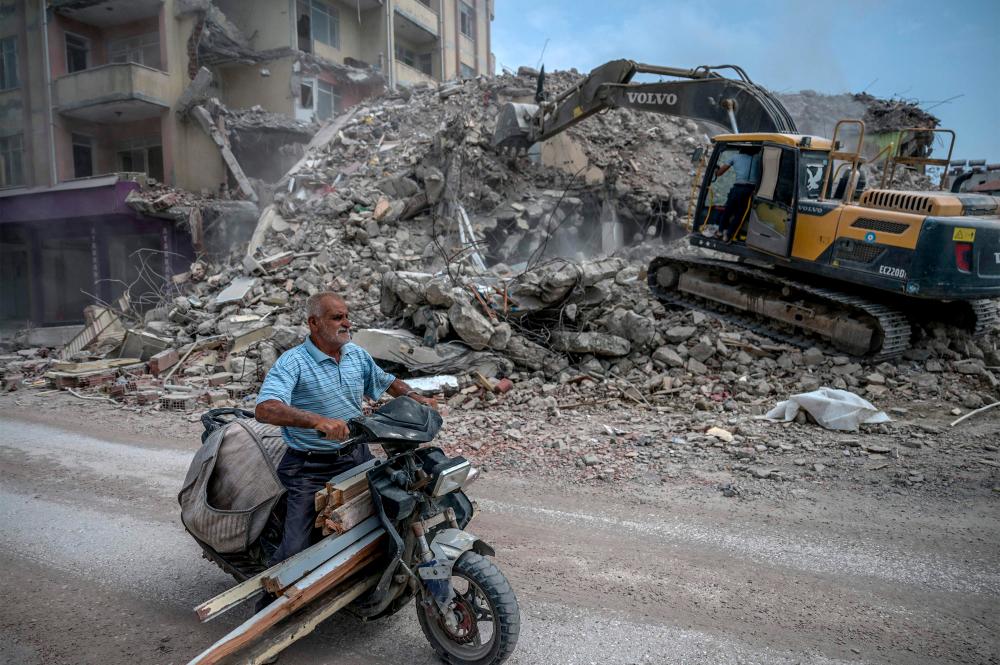 A man rides his motor bike as diggers work to clean the rubble of collapsed buildings//AFPix