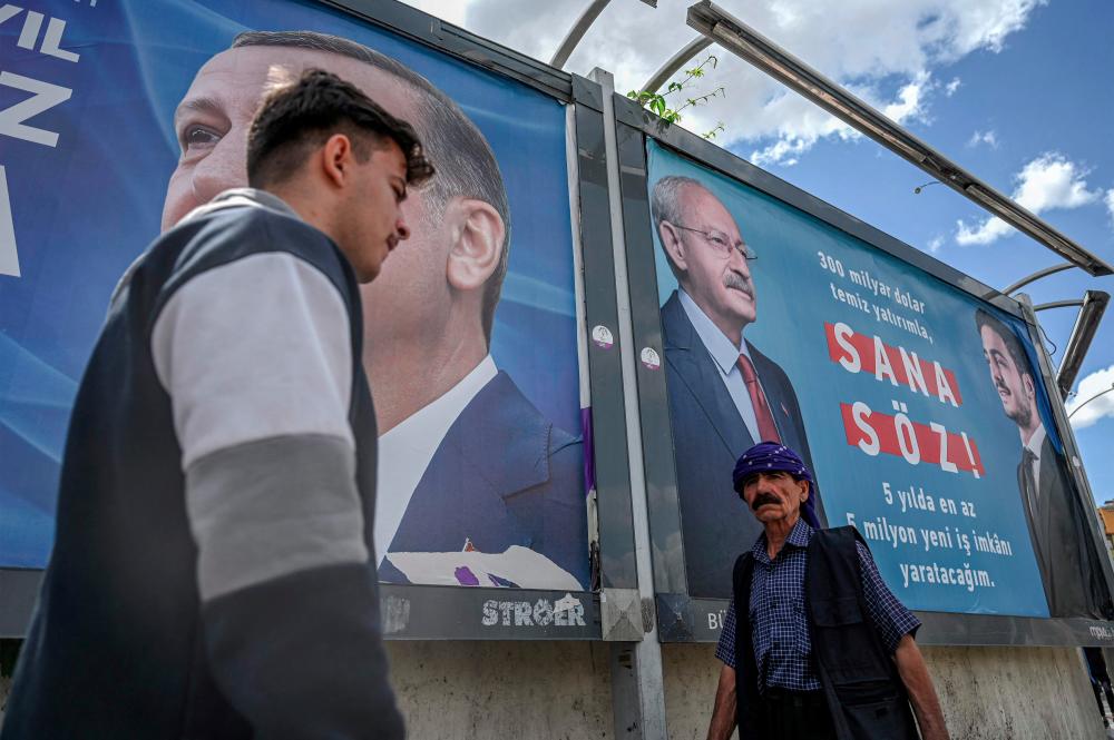 People walk past billboards, one with the portrait of Turkish President Recep Tayyip Erdogan (L) and another with the portrait of Republican People's Party (CHP) leader and presidential candidate, Kemal Kilicdaroglu (R) reading My promise to you in the southwest of the city centre of Sanliurfa on April 28, 2023. AFPPIX