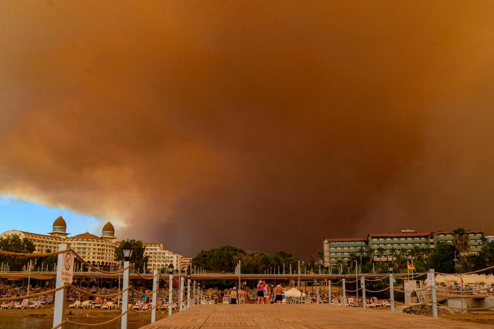 Dark smoke drifts over a hotel complex during a massive forest fire which engulfed a Mediterranean resort region on Turkey's southern coast near the town of Manavgat, on July 29, 2021. At least three people were reported dead on July 29, 2021 and more than 100 injured as firefighters battled blazes engulfing a Mediterranean resort region on Turkey's southern coast. Officials also launched an investigation into suspicions that the fires that broke out Wednesday in four locations to the east of the tourist hotspot Antalya were the result of arson. -AFP