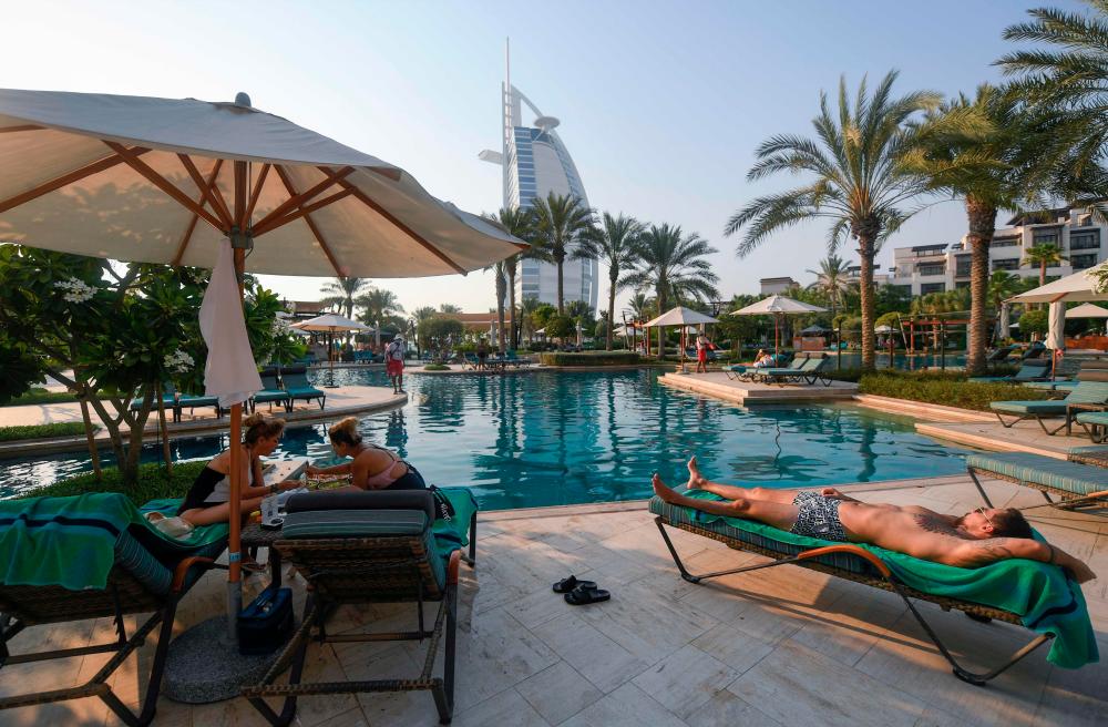 Tourists sunbathe by the pool of the Al Naseem hotel in the Gulf emirate of Dubai in the United Arab Emirates, on July 7, 2020, with a view of the Burj al-Arab hotel in the background. With a “welcome” passport sticker and coronavirus tests on arrival, Dubai reopens its doors to international visitors in the hope of reviving its tourism industry after a nearly four-month closure. / AFP / KARIM SAHIB