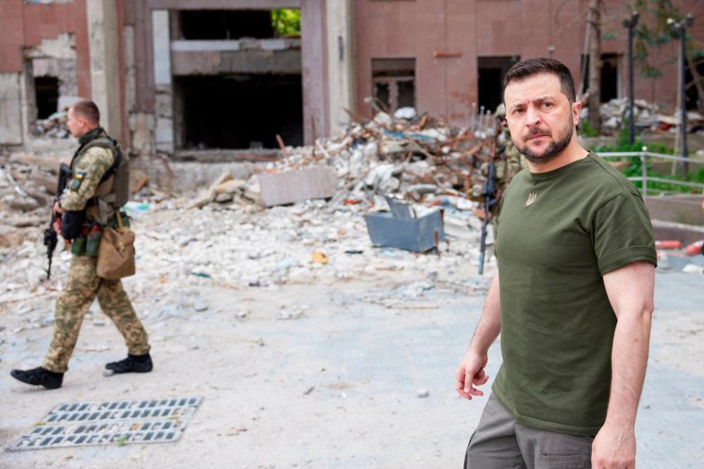 This handout picture taken and released by the press service of the Ukrainian Presidency on 18 June, 2022 shows Ukrainian President Volodymyr Zelensky (R) walking past a partially destroyed building during his visit to the position of Ukrainian troops in Mykolaiv region. AFPPIX