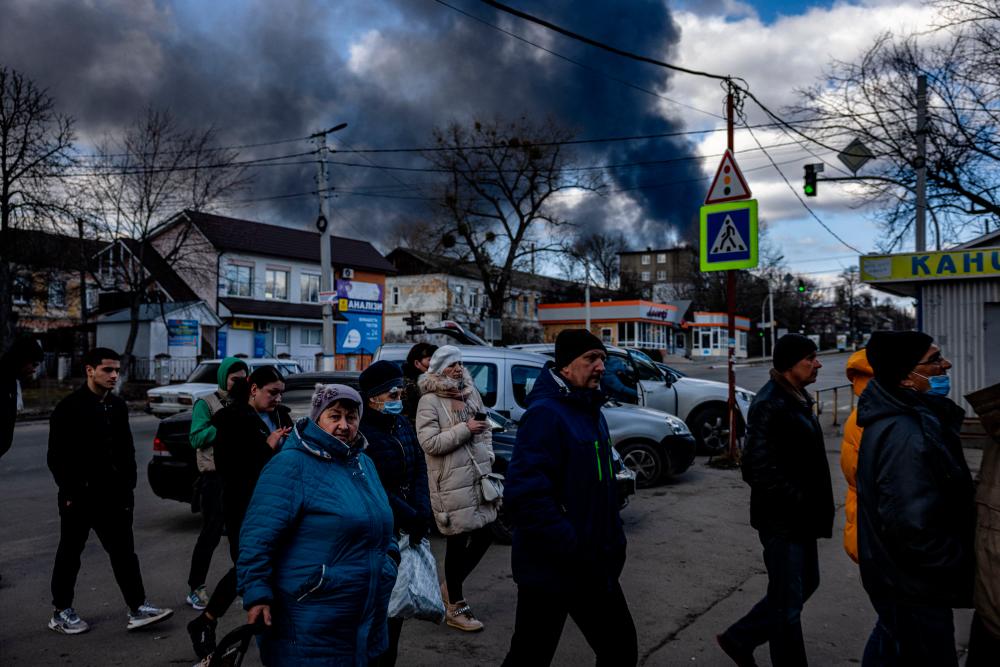 People stand in line in front of a supermarket while smoke billows over the town of Vasylkiv just outside Kiev on February 27, 2022, after overnight Russian strikes hit an oil depot. AFPPIX
