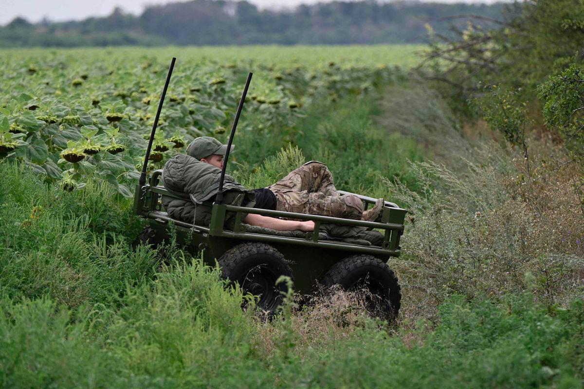 A Ukrainian serviceman, 24, with call sign Bot from the 5th Separate Assault Brigade, rests on the platform of an unmanned ground vehicle during a demonstration of its capabilities on a training ground at an undisclosed location in eastern Ukraine on August 11, 2025, amid the Russian invasion of Ukraine. (Photo by Genya SAVILOV / AFP)