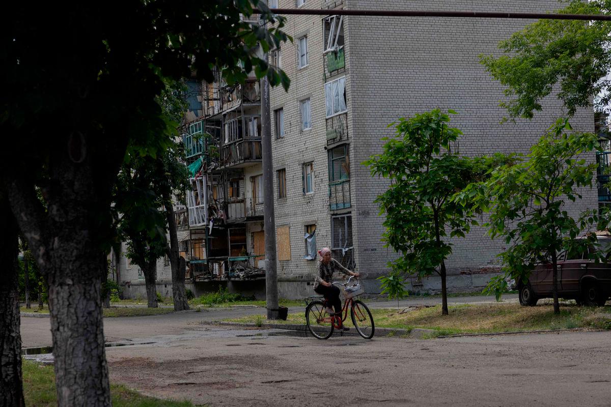 A woman rides a bicycle past a damaged residential building in the town of Lyman, near the frontline in the Donetsk region on June 24, 2025, amid the Russian invasion of Ukraine. (Photo by Tetiana DZHAFAROVA / AFP)