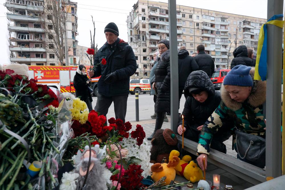 Local residents lay flowers at a bus stop in front of the residential building in the Ukrainian city of Dnipro on January 22, 2023, destroyed as a result of a missile strike on January 14. AFPPIX
