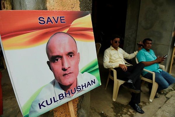 Indian residents sit next to a placard with the picture of Kulbhushan Jadhav, an Indian national convicted of spying in Pakistan, in the neighborhood where he grew up, in Mumbai on July 17, 2019. — afp