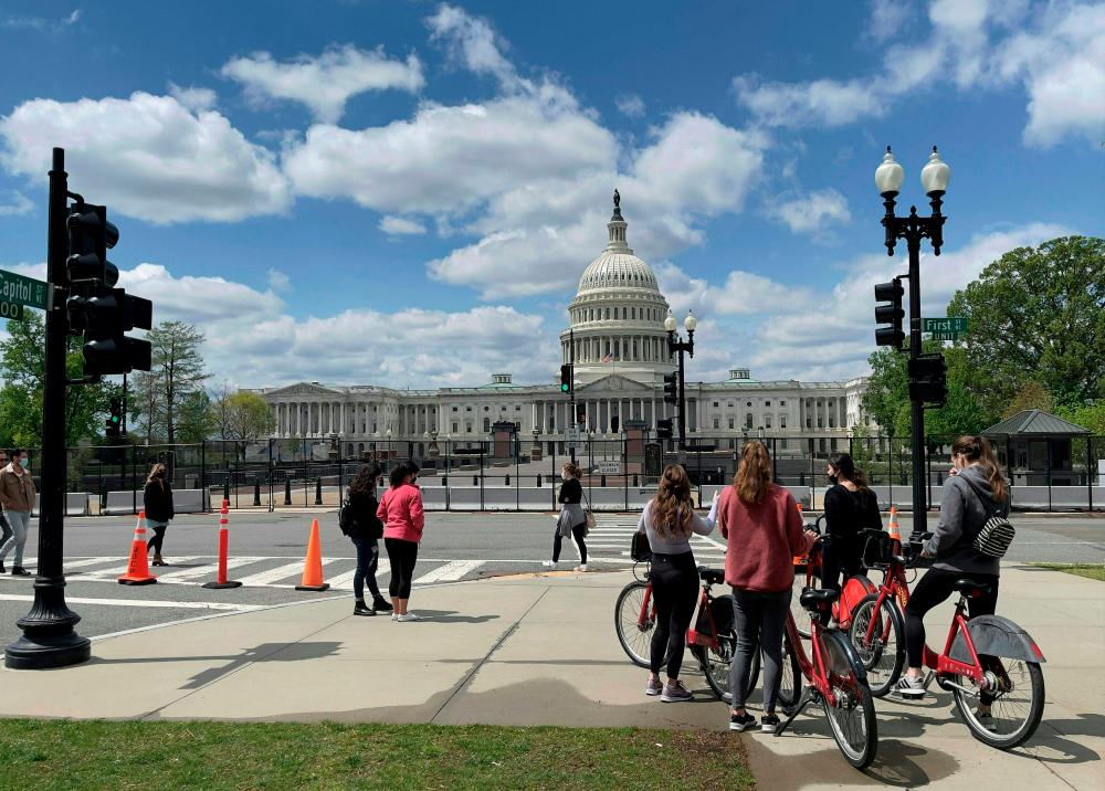 Tourists are seen in front of the security fence surrounding the US Capitol in Washington DC on April 17, 2021. - AFP