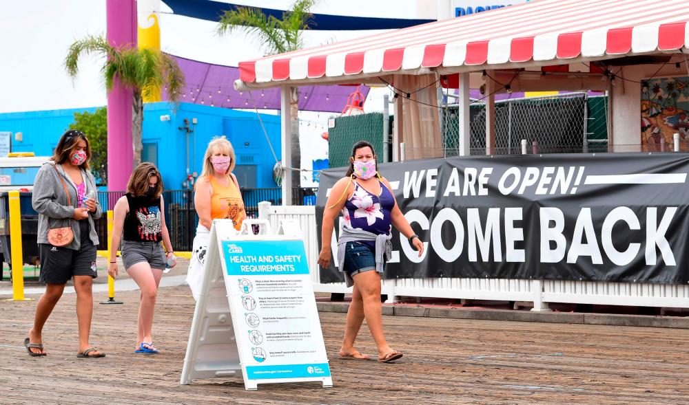 People walk past a health and safety guideline board and an open restaurant on Santa Monica Pier on June 26 in Santa Monica, California. The Conference Board said the lifting of lockdowns to stop the coronavirus pushed the US consumer confidence index above predictions to 98.1 in June. – AFPPIX