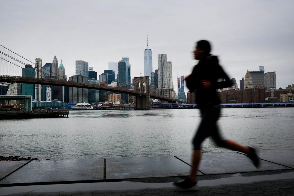 A person runs in Brooklyn while lower Manhattan looms in the background on March 28, 2020 in New York City, NY. — AFP