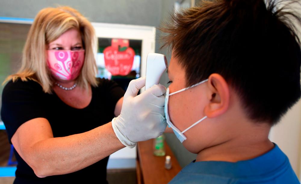 Principal Pam Rasmussen (L) takes the temperature of arriving students as per coronavirus guidelines during summer school sessions at Happy Day School in Monterey Park, California on July 9, 2020. — AFP