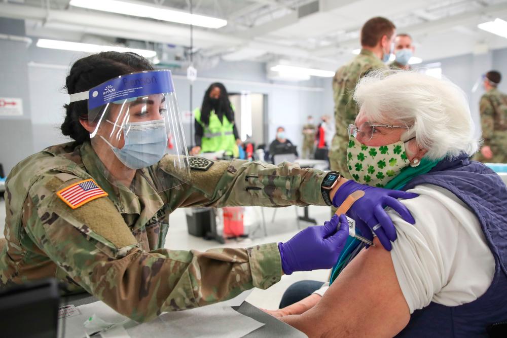 Lucy Y. Powderly (R) receives a Pfizer Covid-19 vaccine from sergeant Julia Benson (L) of the Illinois Army National Guard at a vaccination center established at the Triton College in River Grove, Illinois, on February 3, 2021. The site is the second large-scale vaccination center in Cook County, which includes the city of Chicago. More than 4,000 vaccines are expected to be given at that location on a weekly basis. / AFP / KAMIL KRZACZYNSKI