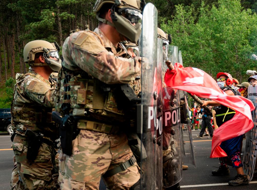 A protester hits the shields of National Guard troops as they block the road to Mount Rushmore National Monument with vans as they protest and confront police and military personnel in Keystone, South Dakota on July 3, 2020, during a demonstration around the Mount Rushmore National Monument and the visit of US President Donald Trump. — AFP