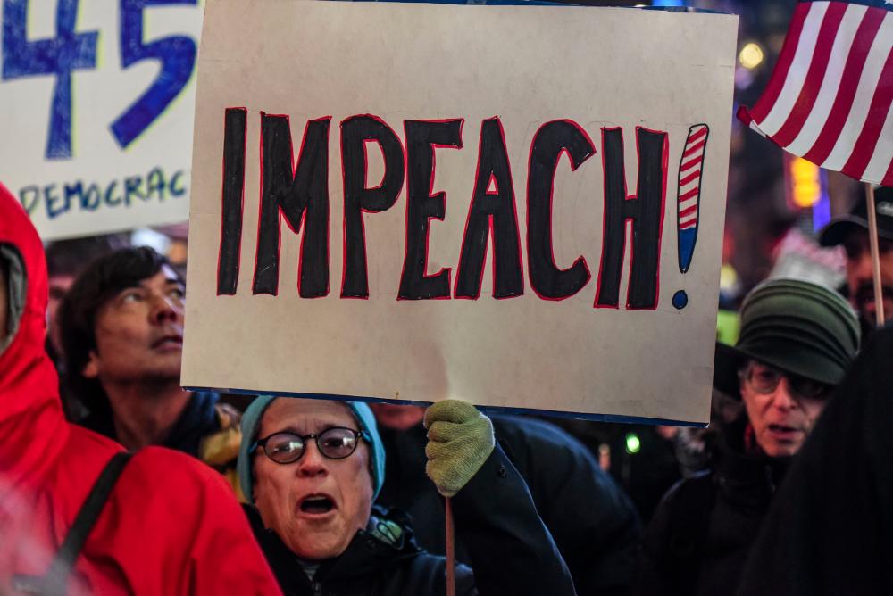 People hold signs critical of US President Donald Trump while participating in a protest in support of his potential impeachment on Dec 17, in New York, United States. — AFP