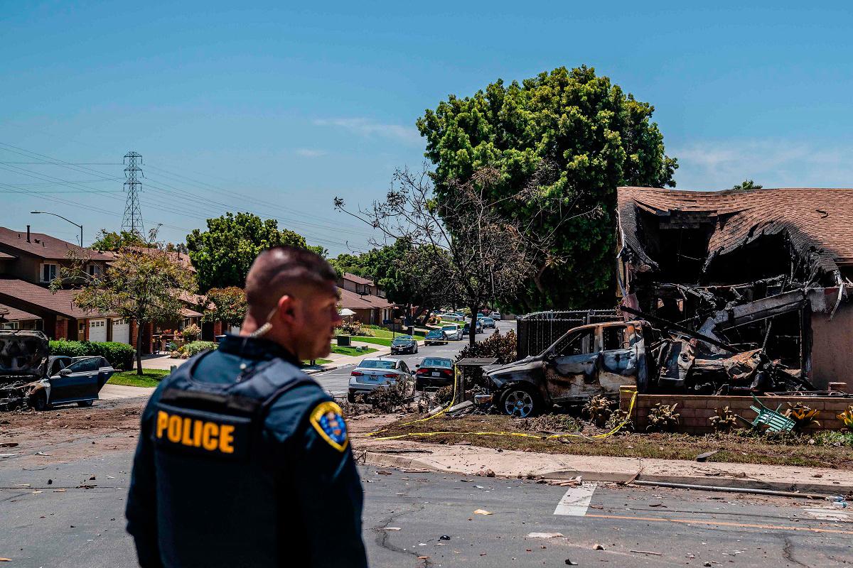 A police officer stands in front of a house that was damaged after a small plane crashed into a neighborhood, setting homes and vehicles on fire on May 22, 2025 in San Diego, California. At least two people have died after a Cessna 550 aircraft crashed into a residential street in Murphy Canyon, causing evacuations after buildings were damaged. - Ariana Drehsler/Getty Images/AFP