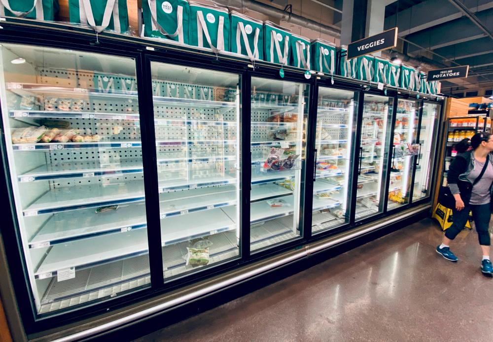 A shopper walks by empty shelves of frozen food in a downtown supermarket on March 11, 2020 in Washington, DC. – AFP