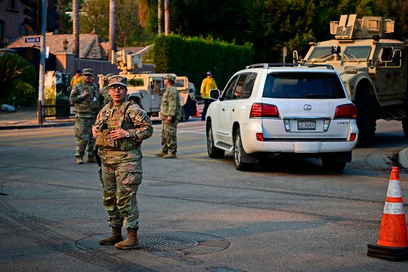 National Guard soldiers stand at a checkpoint to enter the Mandeville Canyon neighborhood of Los Angeles, California, on January 11, 2025, as the Palisades Fire continues to burn. The Palisades Fire, the largest of the Los Angeles fires, spread toward previously untouched neighborhoods January 11, forcing new evacuations and dimming hopes that the disaster was coming under control. Across the city, at least 11 people have died as multiple fires have ripped through residential areas since January 7, razing thousands of homes in destruction that US President Joe Biden likened to a “war scene.” - AGUSTIN PAULLIER / AFP