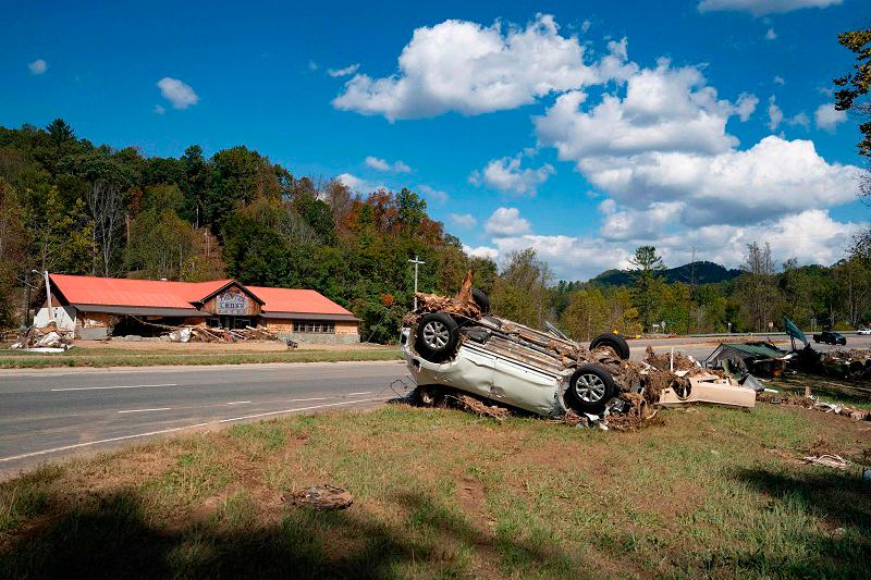 An upside-down car covered by pieces of tree is left on the side of a road in the aftermath of Hurricane Helene in Burnsville, North Carolina, on October 5, 2024. At least 222 people are now confirmed dead after Hurricane Helene carved a path of destruction through several US states, officials said October 5, 2024, making it the second deadliest storm to hit the US mainland in more than half a century. - Allison Joyce / AFP