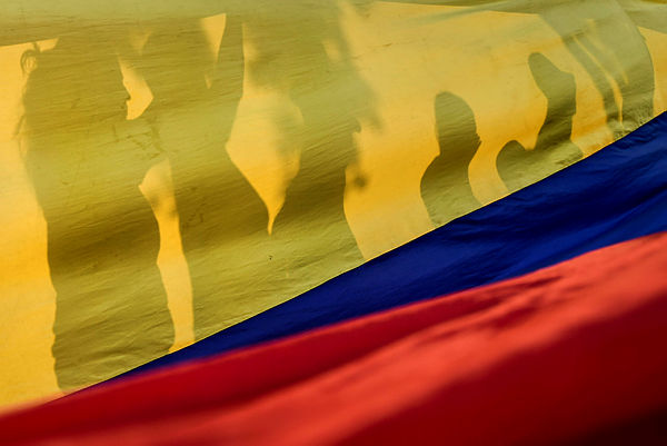 Demostrators are silhouetted against a Venezuelan national flag, during a protest against the government of President Nicolas Maduro at the Santander square in Cucuta, Colombia. — AFP