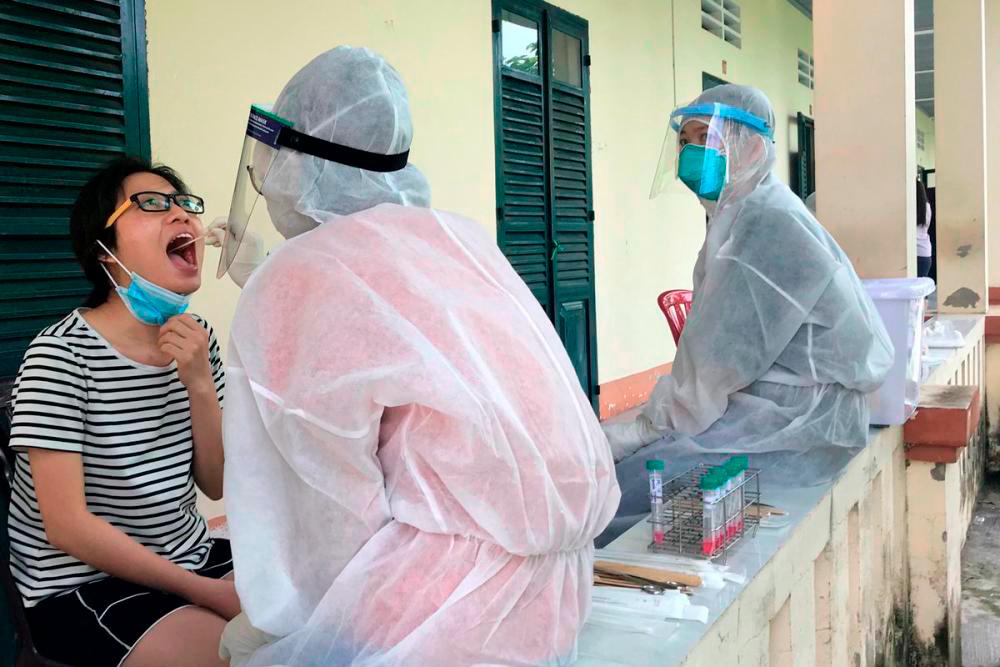 Medical specialists wearing protective hazmat suits take a swab sample to test for the coronavirus disease (Covid-19) from a woman repatriated from Singapore at a military base in southern Mekong delta Dong Thap province, Vietnam/REUTERSpix