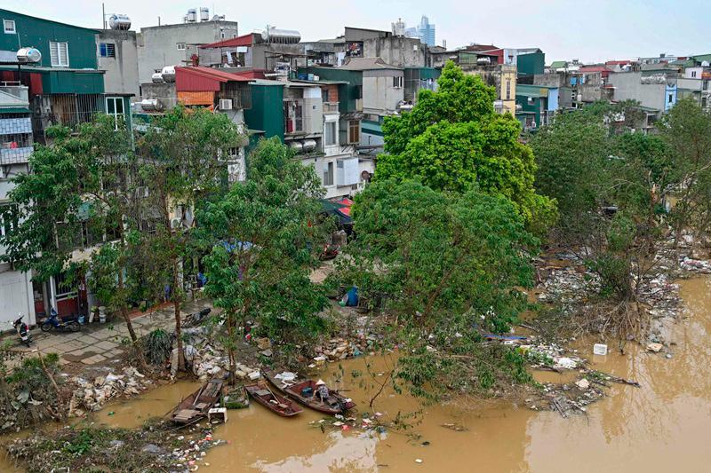 Boats are moored on the bank of the Red River as its high level falls and receding flood waters leave behind debris and garbage in Hanoi on September 13, 2024. Typhoon Yagi brought a colossal deluge of rain that has inundated a swathe of northern Vietnam, Laos, Thailand and Myanmar, triggering deadly landslides and widespread river flooding. - Nhac NGUYEN / AFP