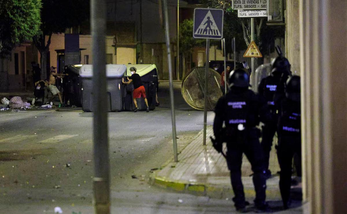 People move dumpsters on a road as police officers keep watch, amid anti-migrant unrest following an attack on an elderly man by unknown assailants earlier in the week, in Torre Pacheco, Spain, July 13, 2025. REUTERS/Violeta Santos Moura