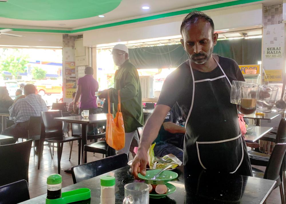 A worker at a food court in Kuala Lumpur clearing a table. He is seen wearing an apron but without a cap, gloves and a facemask as required./Syazwan Kamal/SunPix