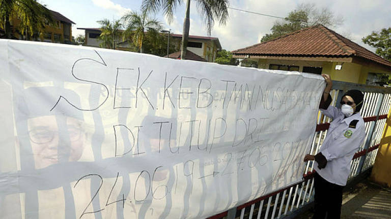 Filepix taken on June 24 shows a security guard hanging up a notice to inform of the school’s temporary closure at Sekolah Kebangsaan (SK) Taman Nusa Damai, Pasir Gudang.
