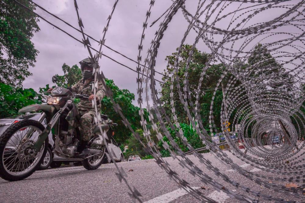 $!TIGHT SECURITY... A soldier standing guard alongside barbed wires at Kampung Sungai Penchala in Kuala Lumpur, which was placed under enhanced movement control. - ADIB RAWI YAHYA/THESUN