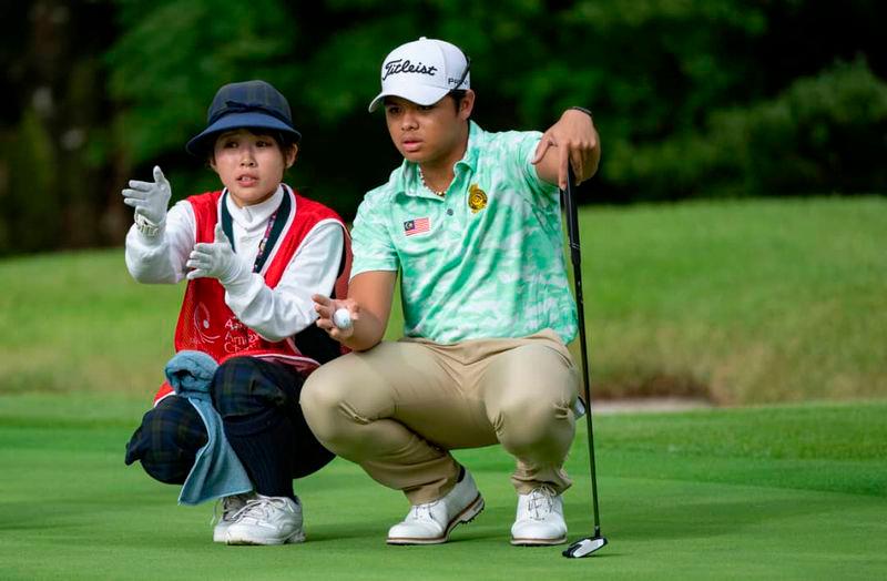 Malaysia’s Rizq Adam Rohizam reads a putt with the help of his caddie