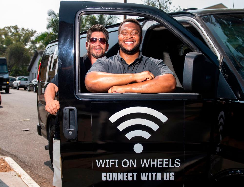 Roman Reyna (L) owner of JFK transportation and Kevin Watson (R), president of JFK transportation, pose with one of their company vans equipped as a mobile Wifi Hotspot to help students access internet to remotely attend their classes, September 16, 2020, in Santa Ana, California. A minivan with a Wi-fi router attached to the dashboard and a satellite antenna on the roof is helping 200 disadvantaged students in Santa Ana, close to Los Angeles, cope with the rigors of distance learning during the coronavirus pandemic. -AFP
