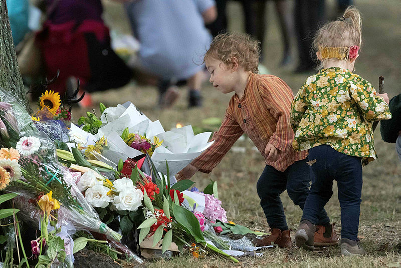 A small child adds a flower to tributes across the road at the Masjid Al Noor mosque on March 19, 2019 in Christchurch, New Zealand, where worshippers were gunned down three days ago. — AFP