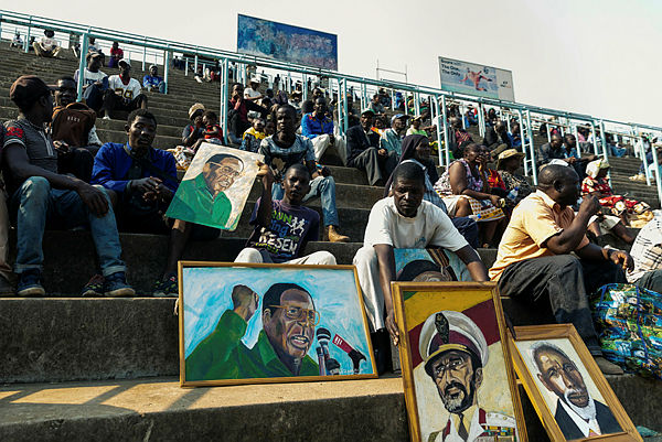 An artist sits among portraits, among them some of late former Zimbabwe president Robert Mugabe, as people gather for viewing the body of Robert Mugabe lying in state during a public send off at the Rufaro Stadium in Harare on Sept 13, 2019. — AFP